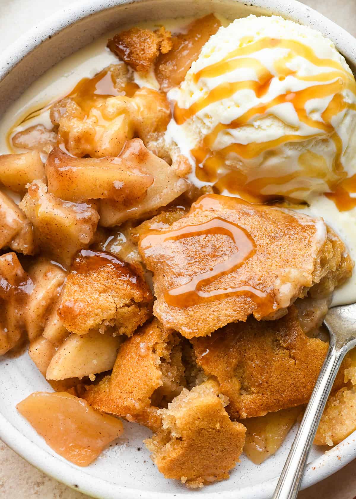 apple cobbler in a bowl with a spoon, vanilla ice cream and caramel sauce