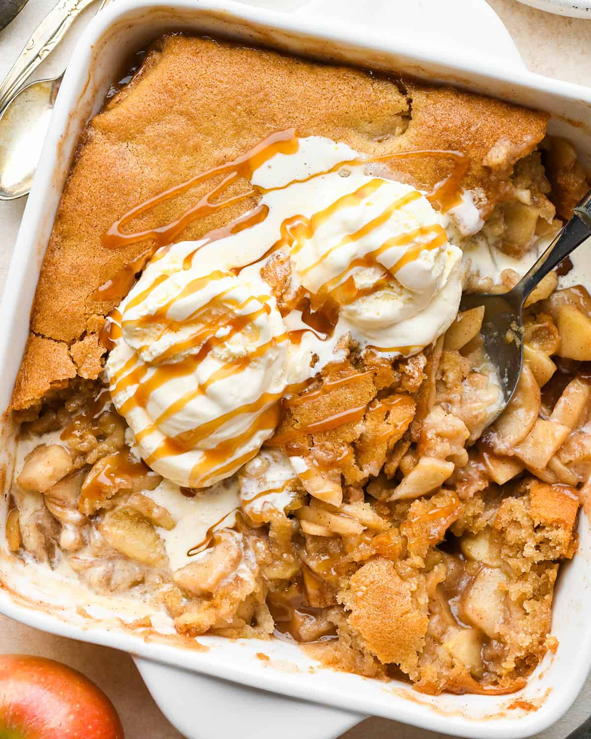 Apple Cobbler in a baking dish with vanilla ice cream, caramel sauce and a spoon