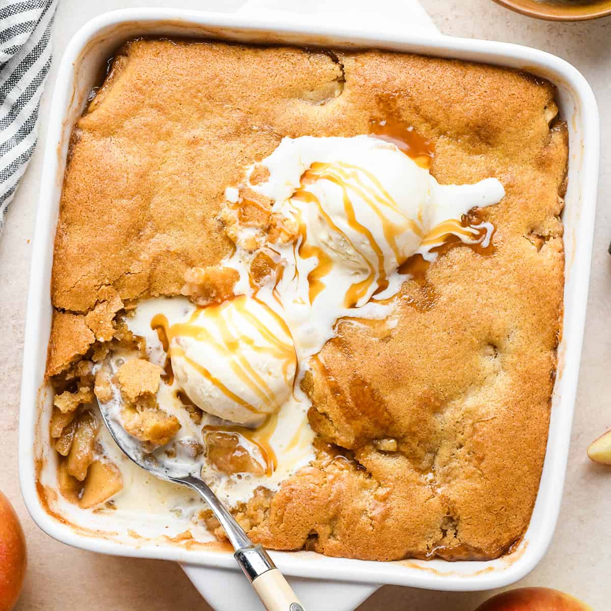 Apple Cobbler in a baking dish with vanilla ice cream, caramel sauce and a spoon