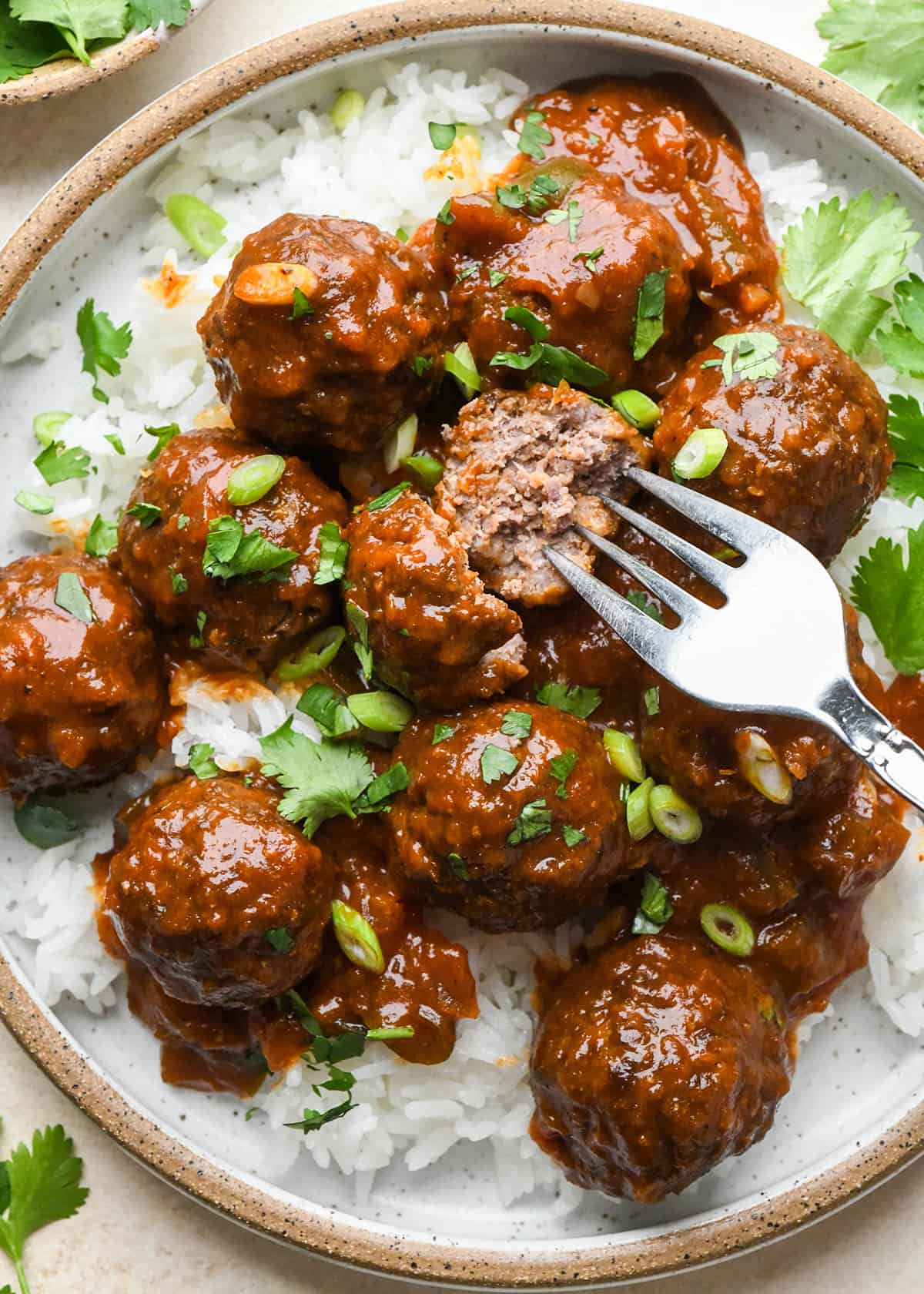 BBQ Meatballs on a plate over rice, one cut in half with a fork. 