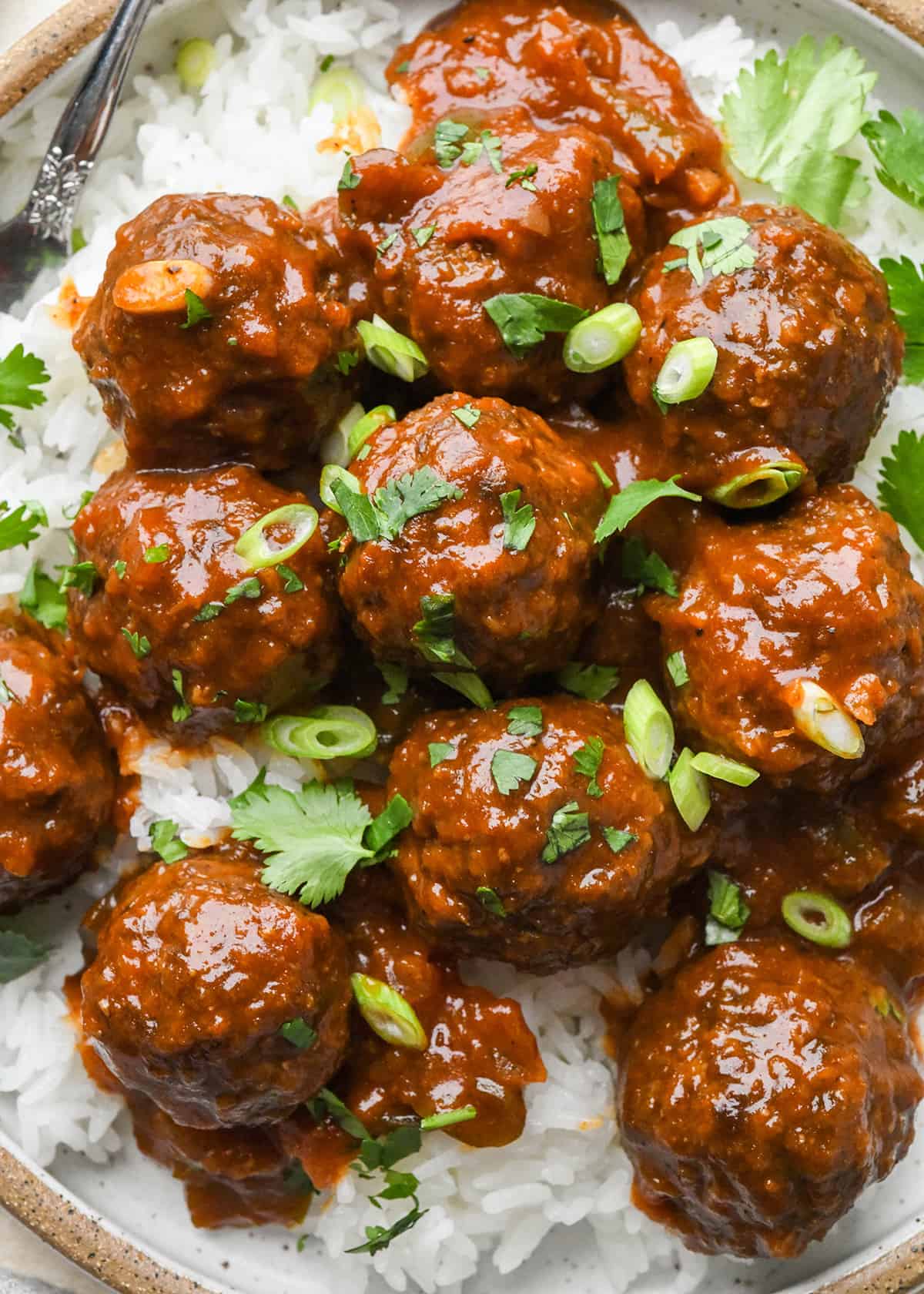 BBQ Meatballs over rice on a plate garnished with cilantro and green onions