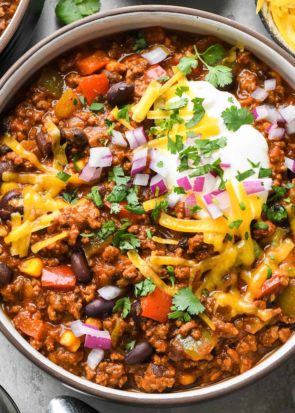 Crock Pot Chili in a bowl garnished with sour cream, cheese, cilantro and red onions 