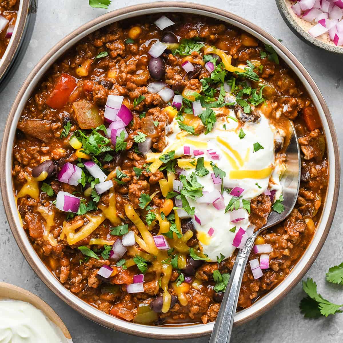 a spoon in a bowl of Crock Pot Chili garnished with sour cream cheese and cilantro