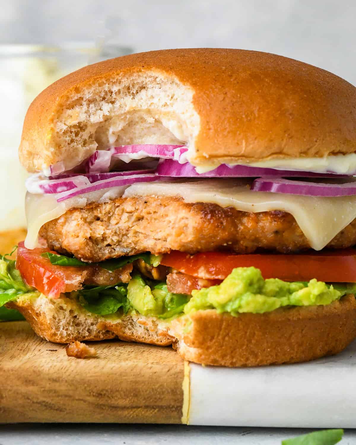 a Chicken Burger on a bun with toppings and a bite taken out of it