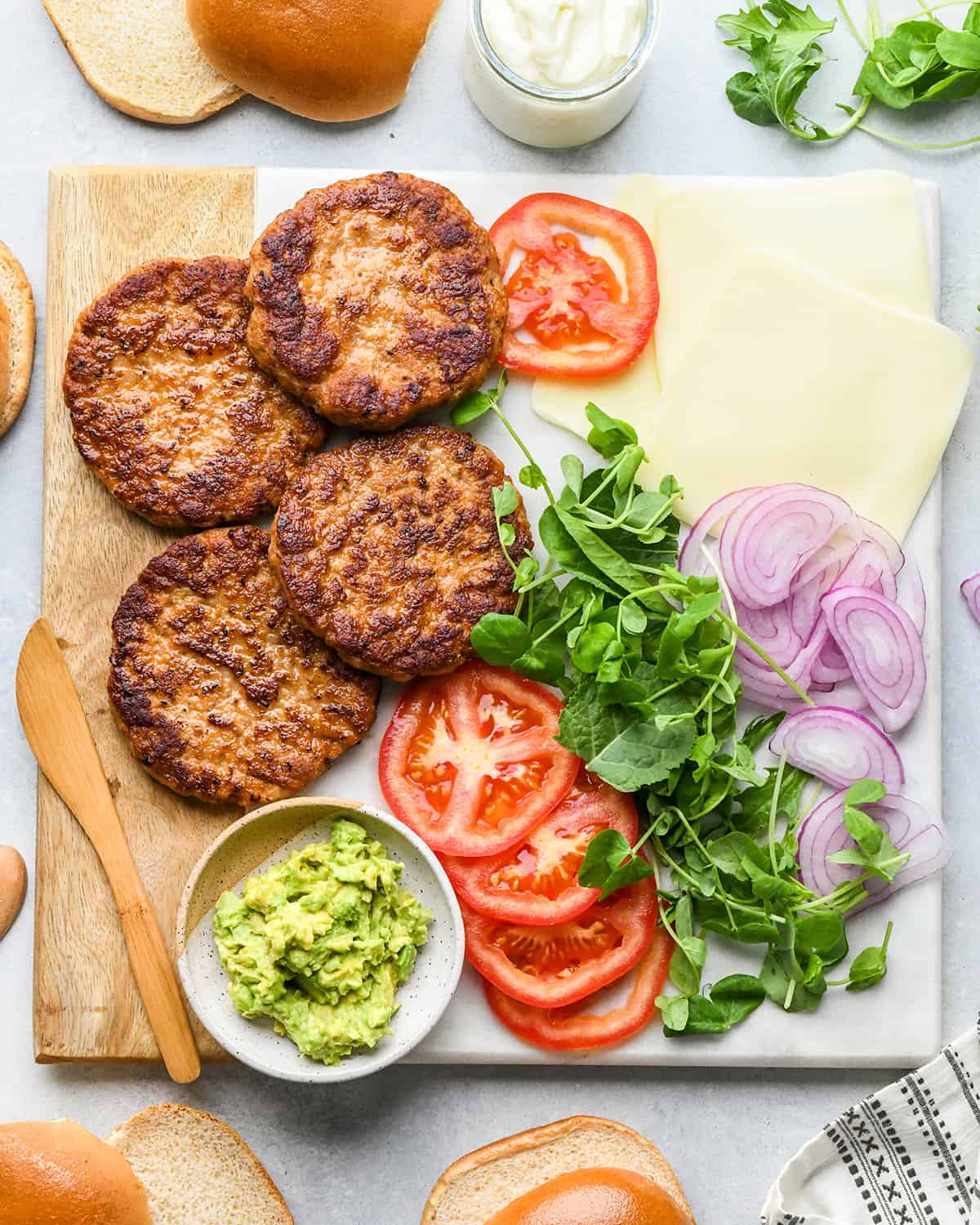 4 Chicken Burgers on a serving platter with toppings like cheese, tomato, lettuce onion and avocado. 