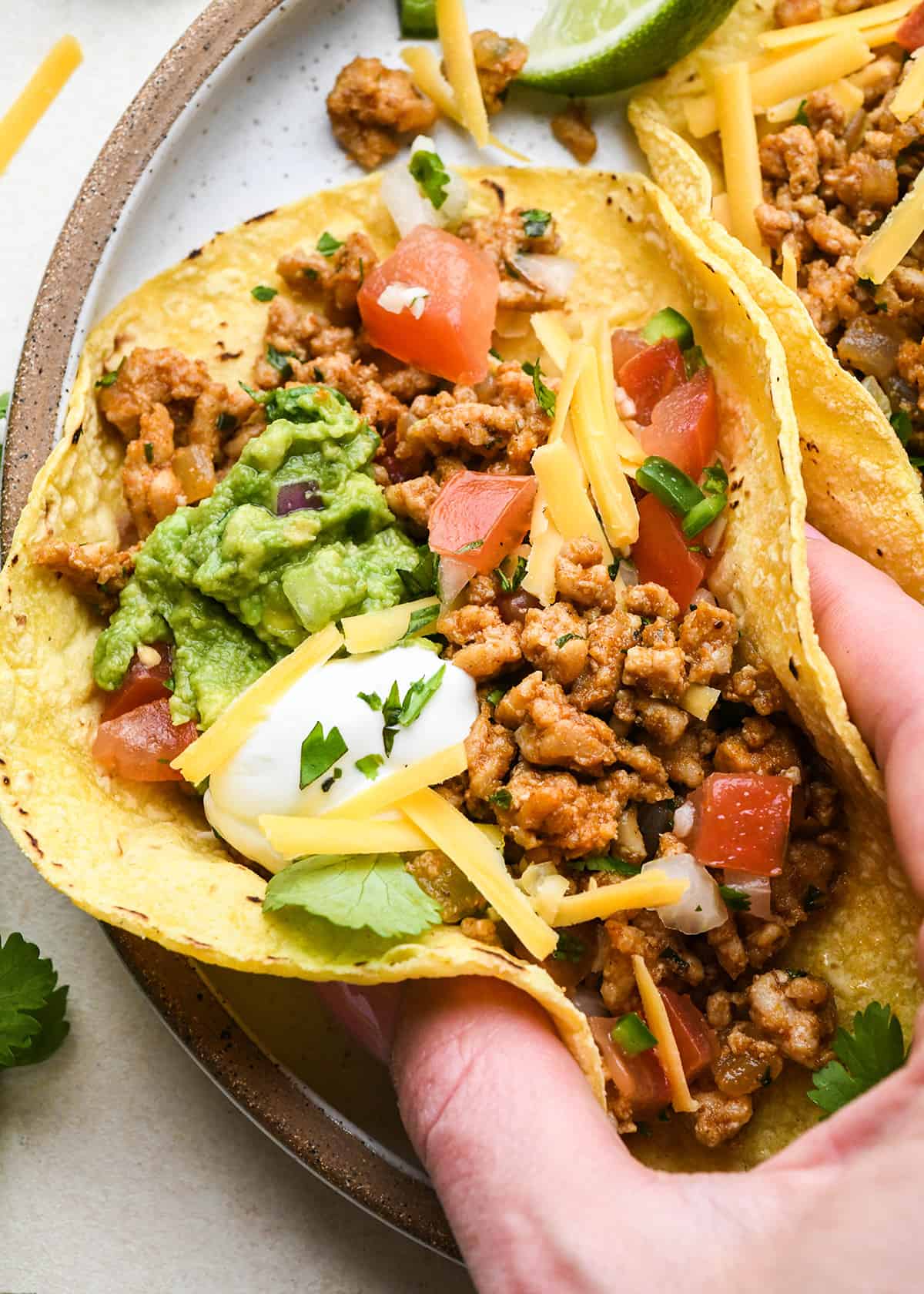 a hand picking up a Ground Chicken Taco from a plate