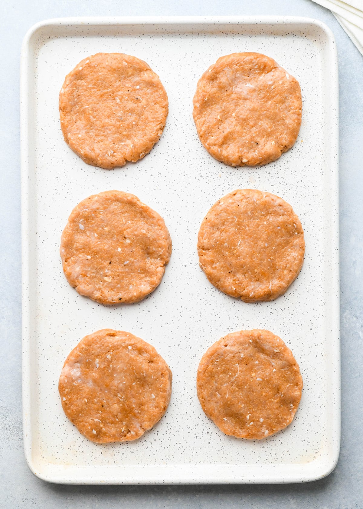 6 chicken burger patties on a baking sheet before cooking