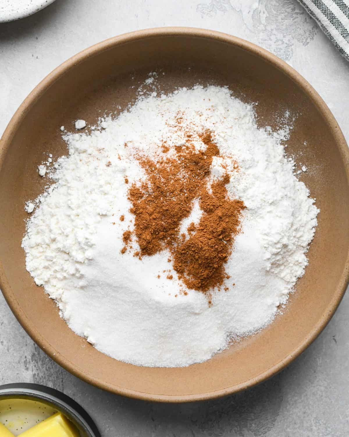 making crumble topping for apple pie - flour, sugar, cinnamon and salt in a brown mixing bowl on a gray surface before mixing