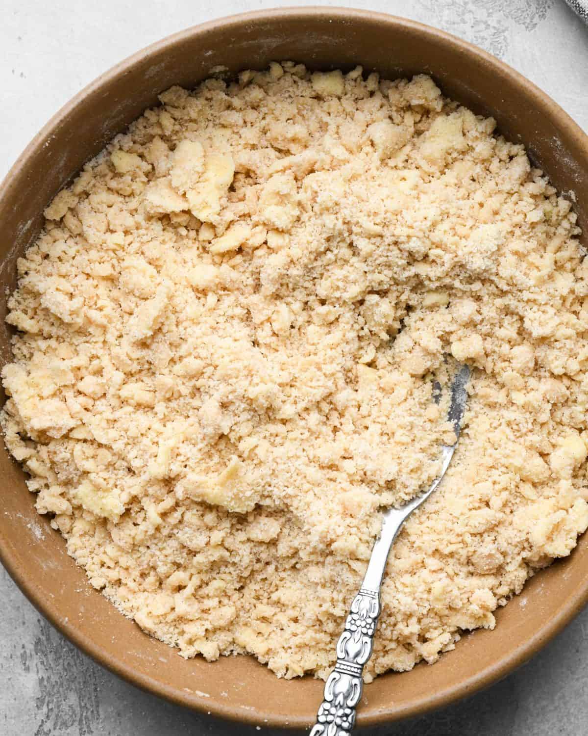 crumble topping for apple pie in a brown mixing bowl with a silver fork