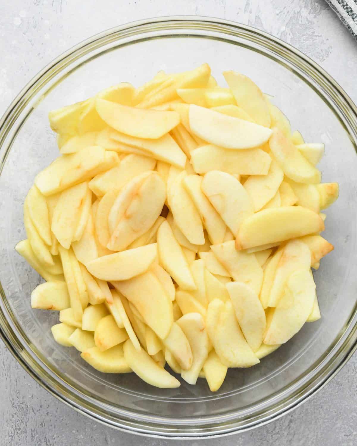 making apple crumb pie - sliced and peeled apples in a glass mixing bowl on a gray surface after cooking