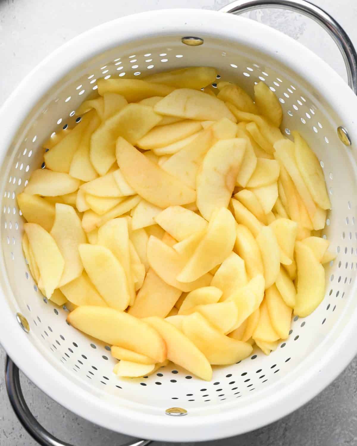 making apple crumb pie - partially cooked, sliced and peeled apples in a white colander draining off excess water