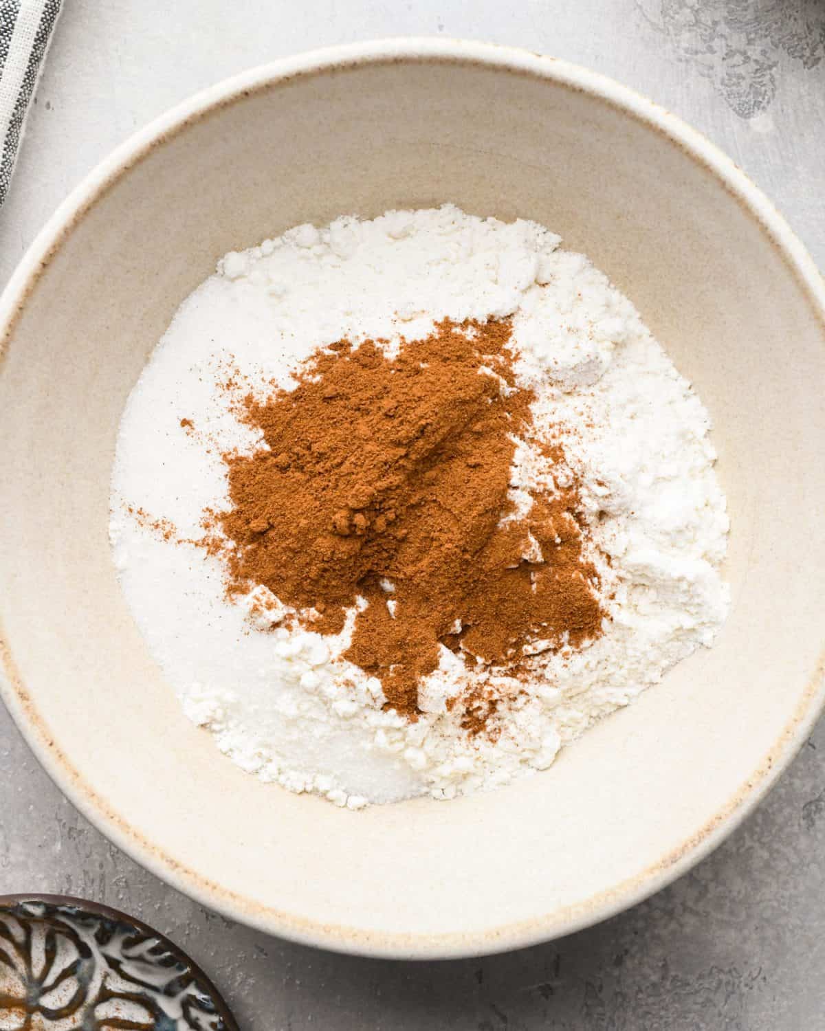 making apple crumb pie - cinnamon, sugar, nutmeg, flour and salt in a ceramic bowl on a gray surface before mixing