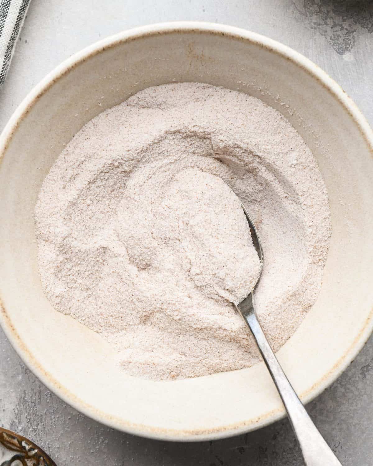 making apple crumb pie - dry filling ingredients in a ceramic mixing bowl with a silver spoon on a gray surface after mixing