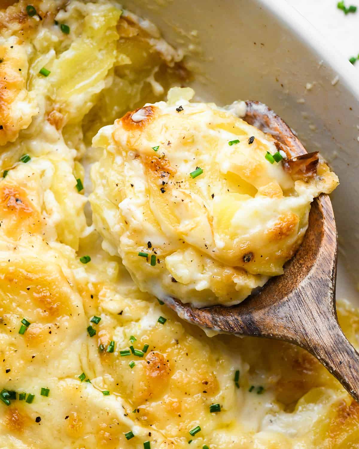 a wooden spoon scooping Scalloped Potatoes out of a baking dish