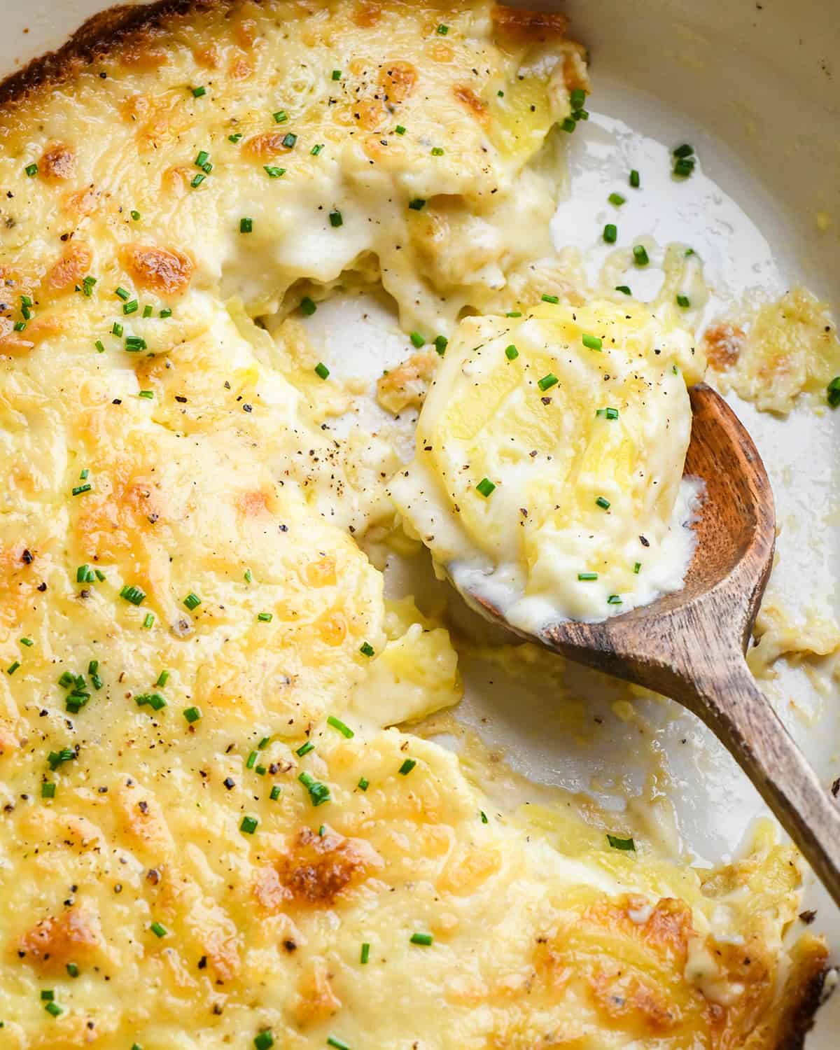 a wooden spoon scooping Scalloped Potatoes out of a baking dish