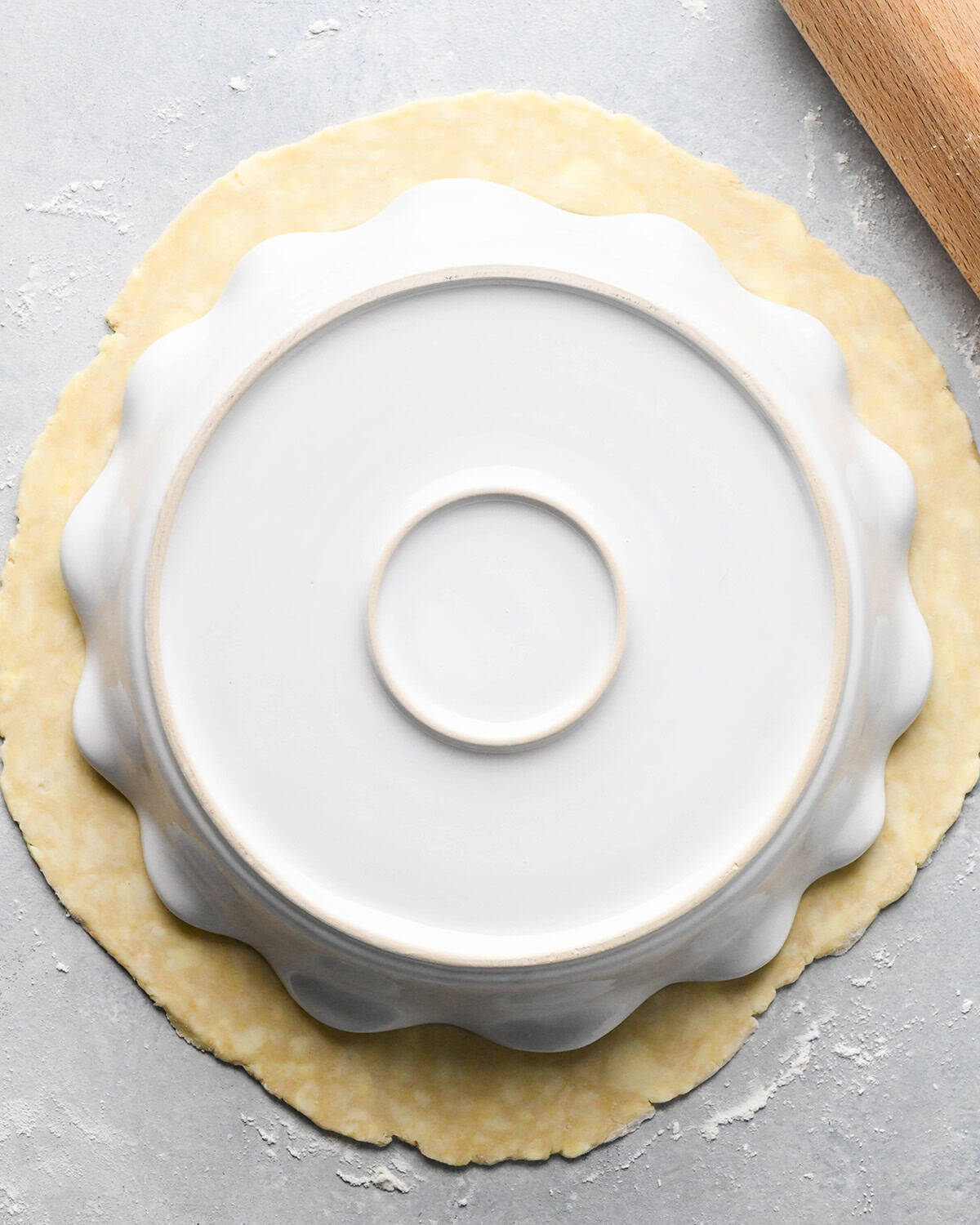 making apple crumb pie - pie crust rolled out with a pie dish on top to measure the size on a gray surface with a wood rolling pin in the top right corner