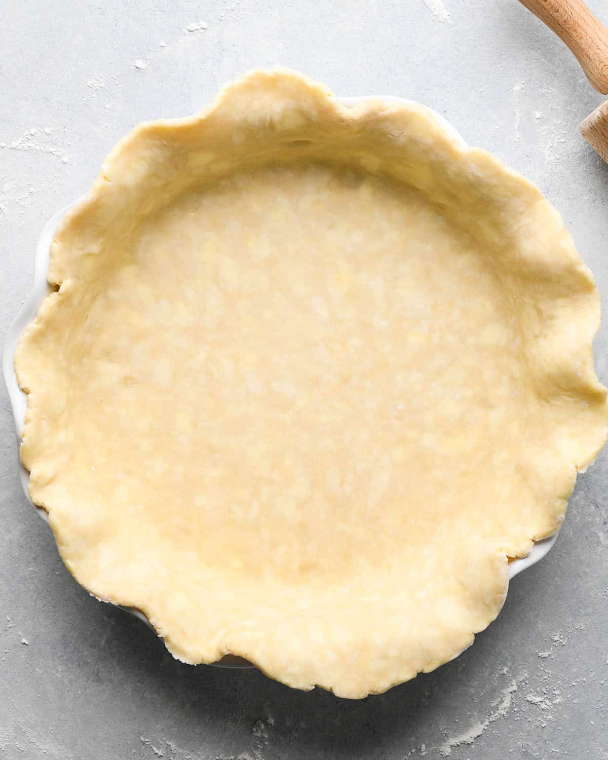 making apple crumb pie - pie crust in a white pie dish on a gray surface with a wood rolling pin in the top right corner