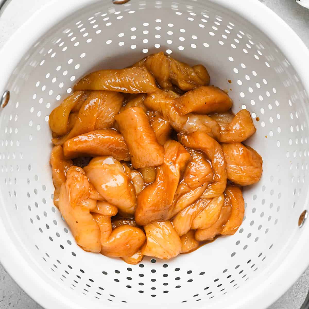 marinated chicken draining in a colander