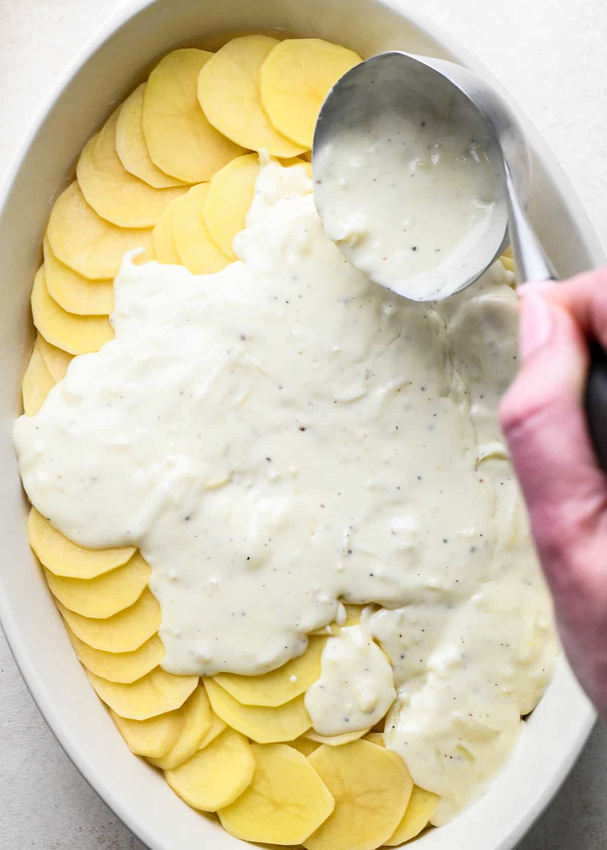 How to Make Scalloped Potatoes - pouring sauce over potatoes in the baking dish