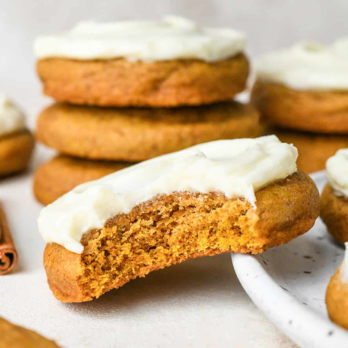 a pumpkin cookie with cream cheese frosting with a bite taken out of it 