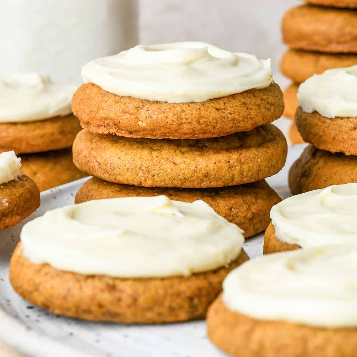 a stack of 3 Pumpkin Cookies with Cream Cheese Frosting surrounded by other pumpkin cookies