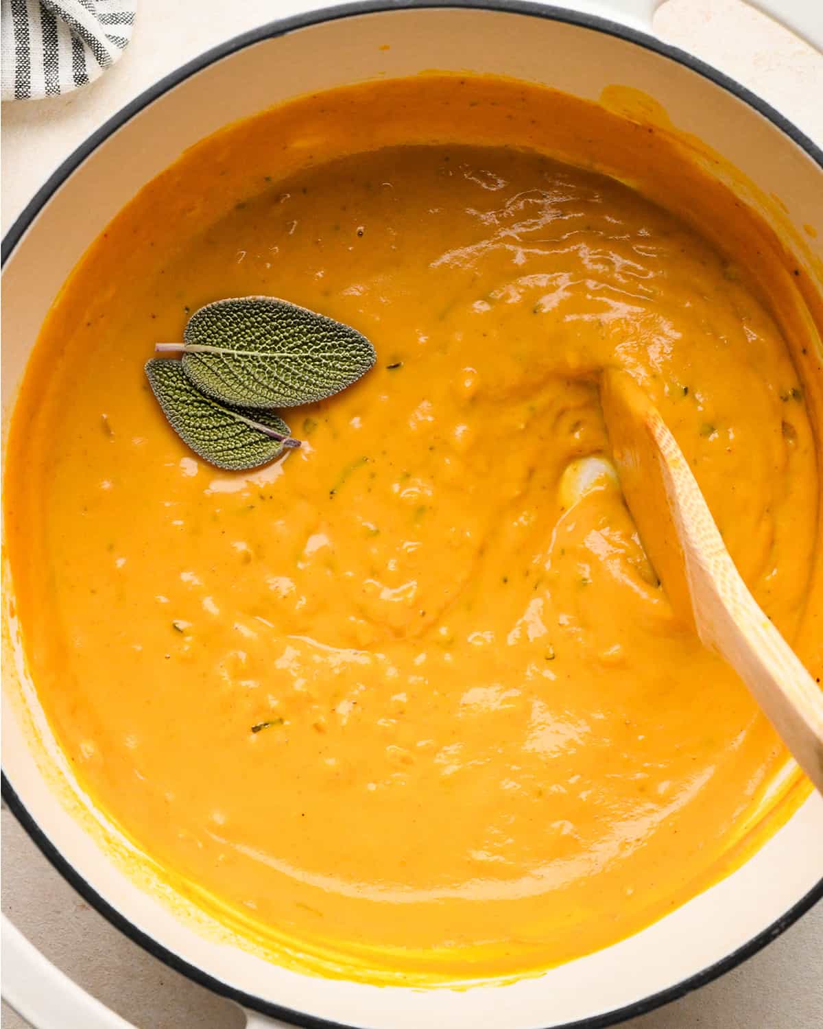 Pumpkin Pasta sauce in a pot with sage and a wooden spoon