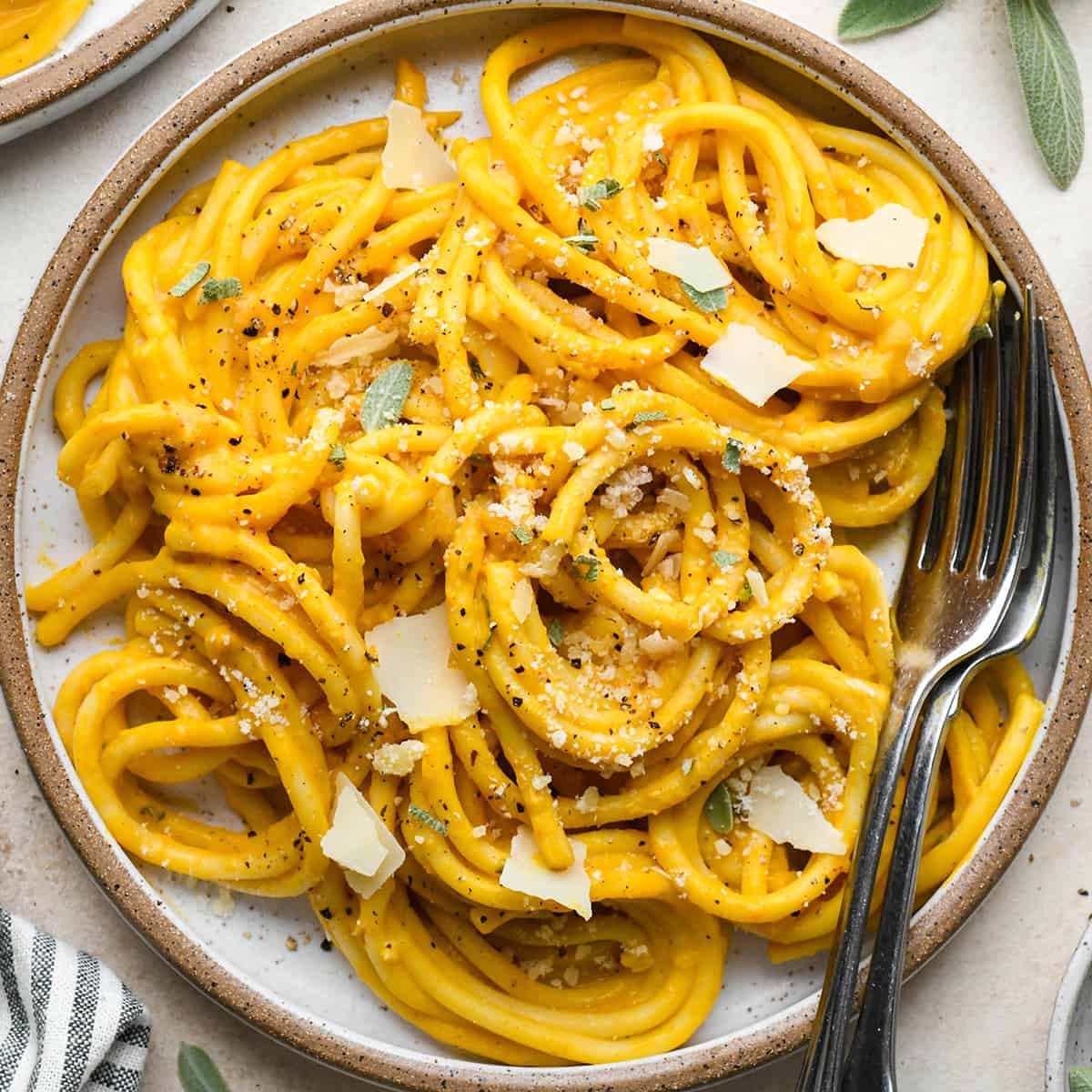 Pumpkin Pasta on a plate with two forks, garnished with parmesan and sage. 