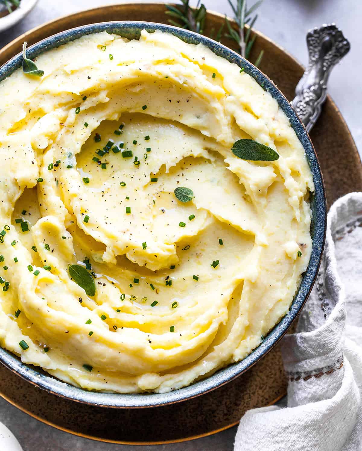 Best Mashed Potatoes Recipe in a serving bowl topped with butter and herbs