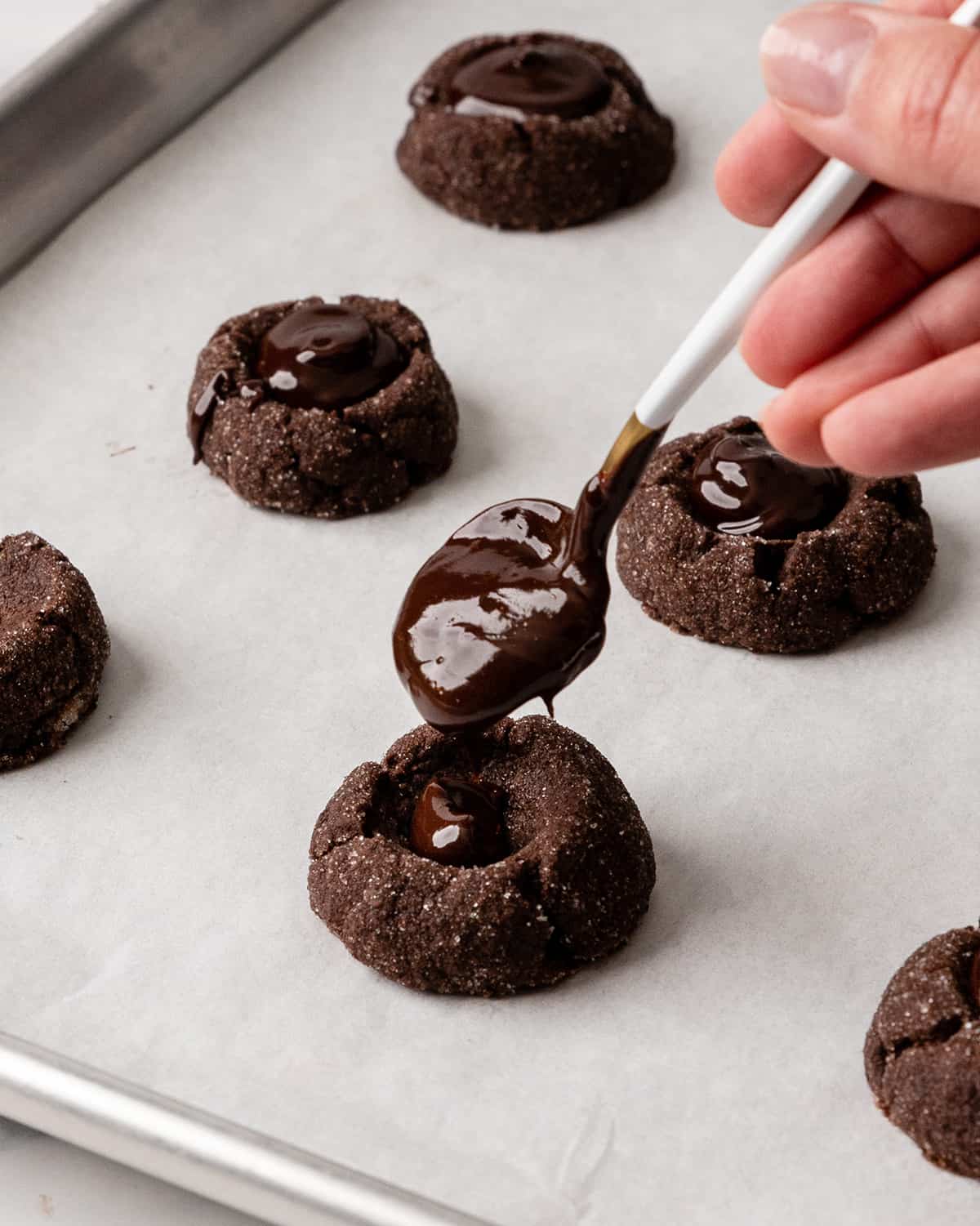 adding the chocolate ganache to baked chocolate thumbprint cookies