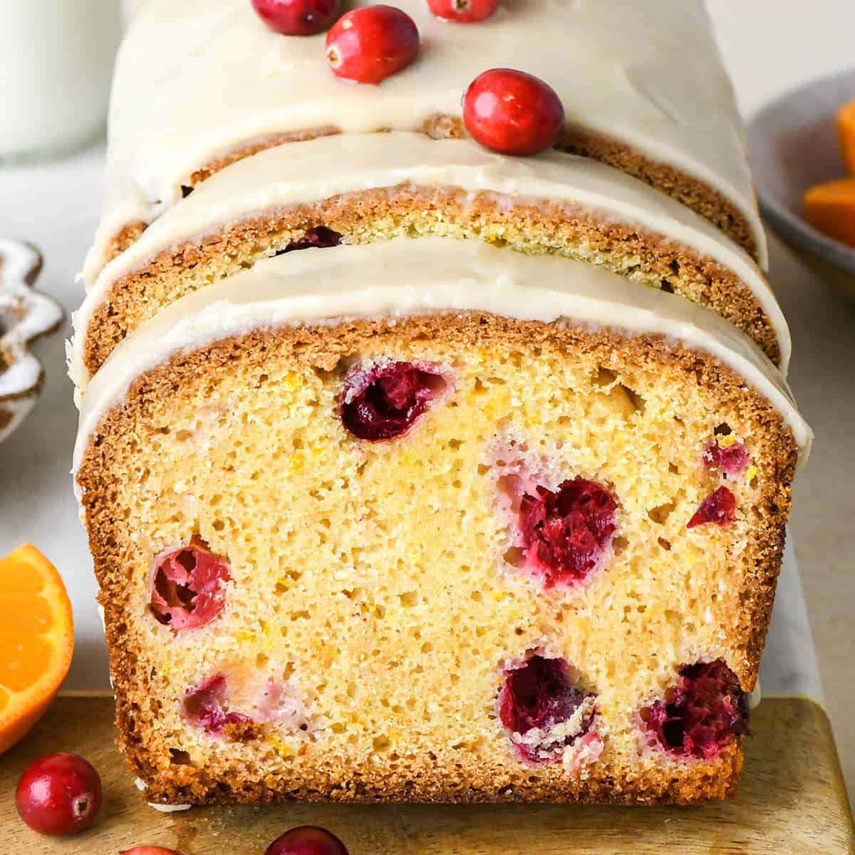 a loaf of Cranberry Orange Bread with glaze and two slices cut out of it