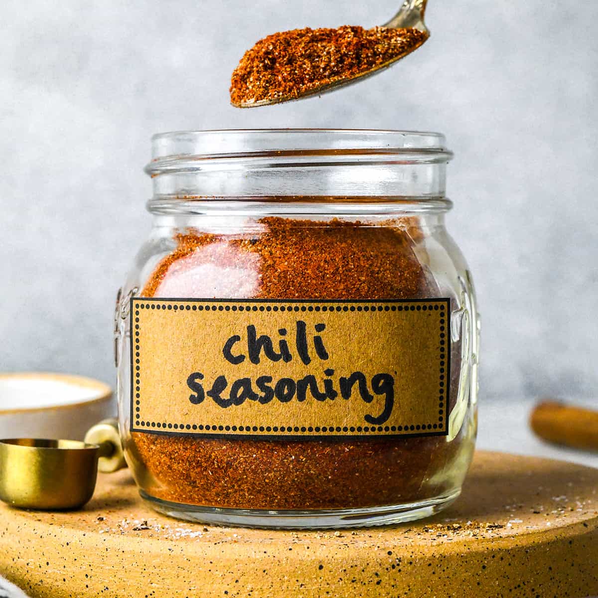 a spoon taking a scoop of Homemade Chili Seasoning Recipe out of a jar labeled "chili seasoning"