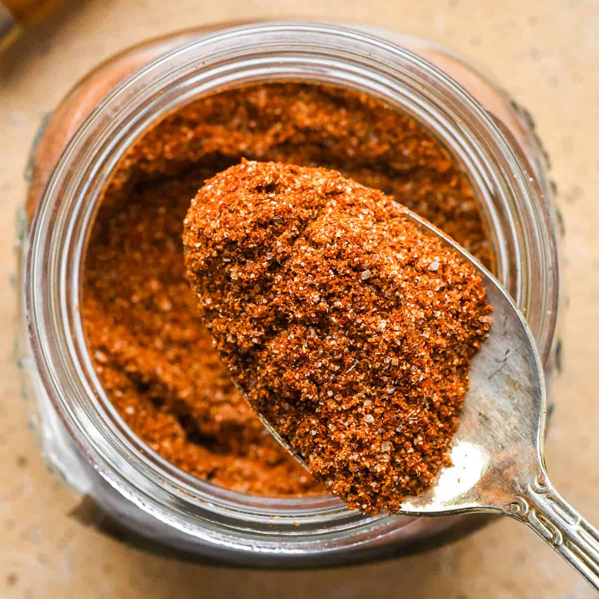 up close overhead photo of a spoon taking a scoop of chili seasoning out of a glass jar