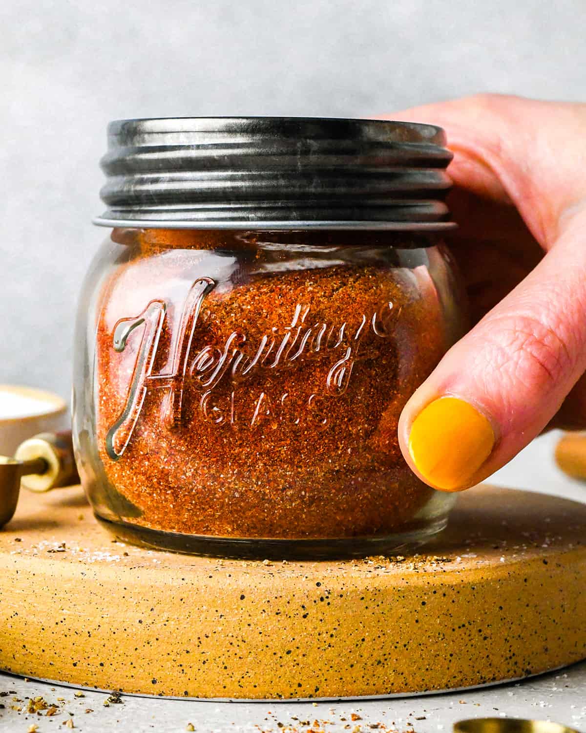 a hand holding a glass jar with chili seasoning ingredients inside and a lid on after shaking to mix the ingredients