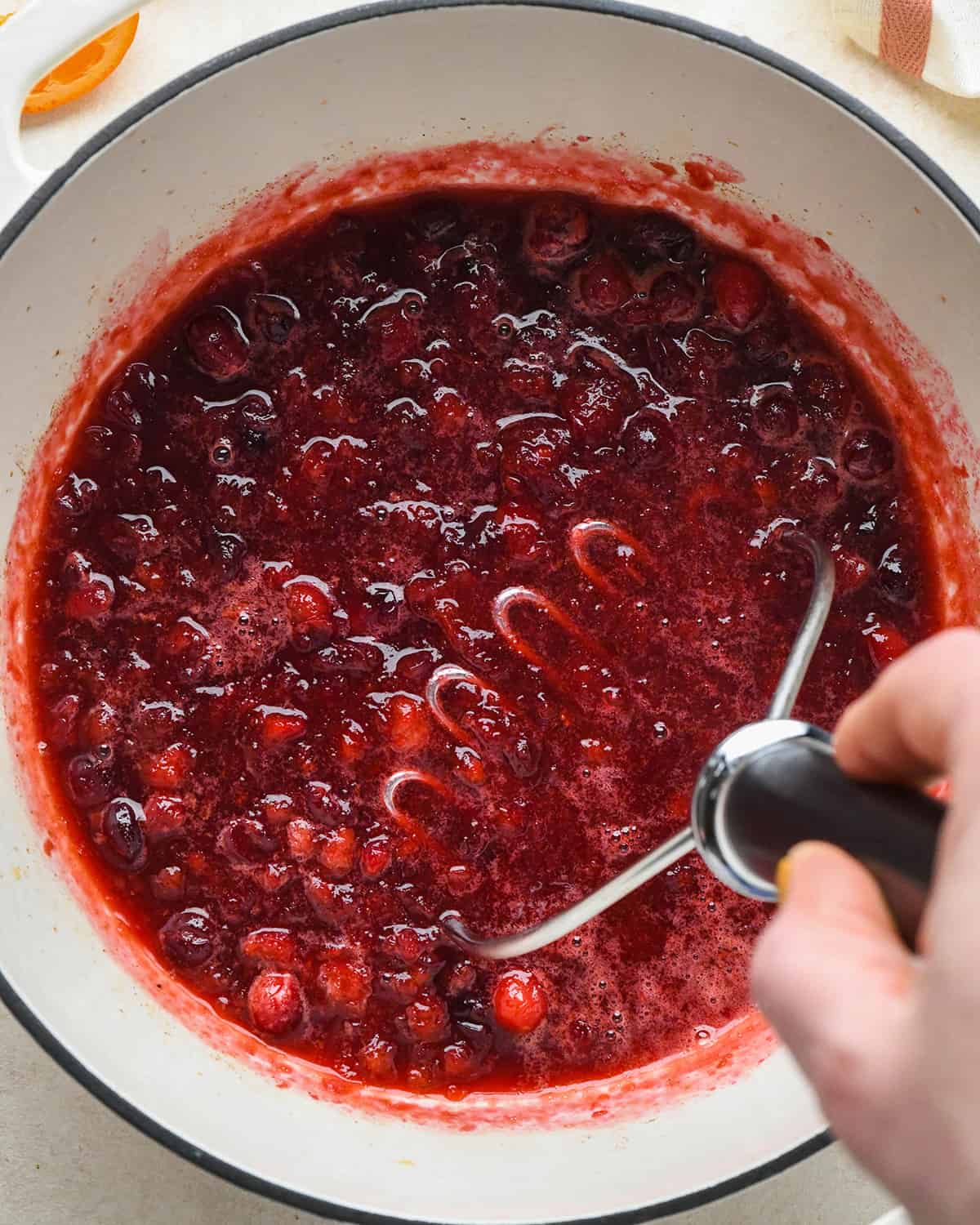 a potato masher mashing cranberry sauce