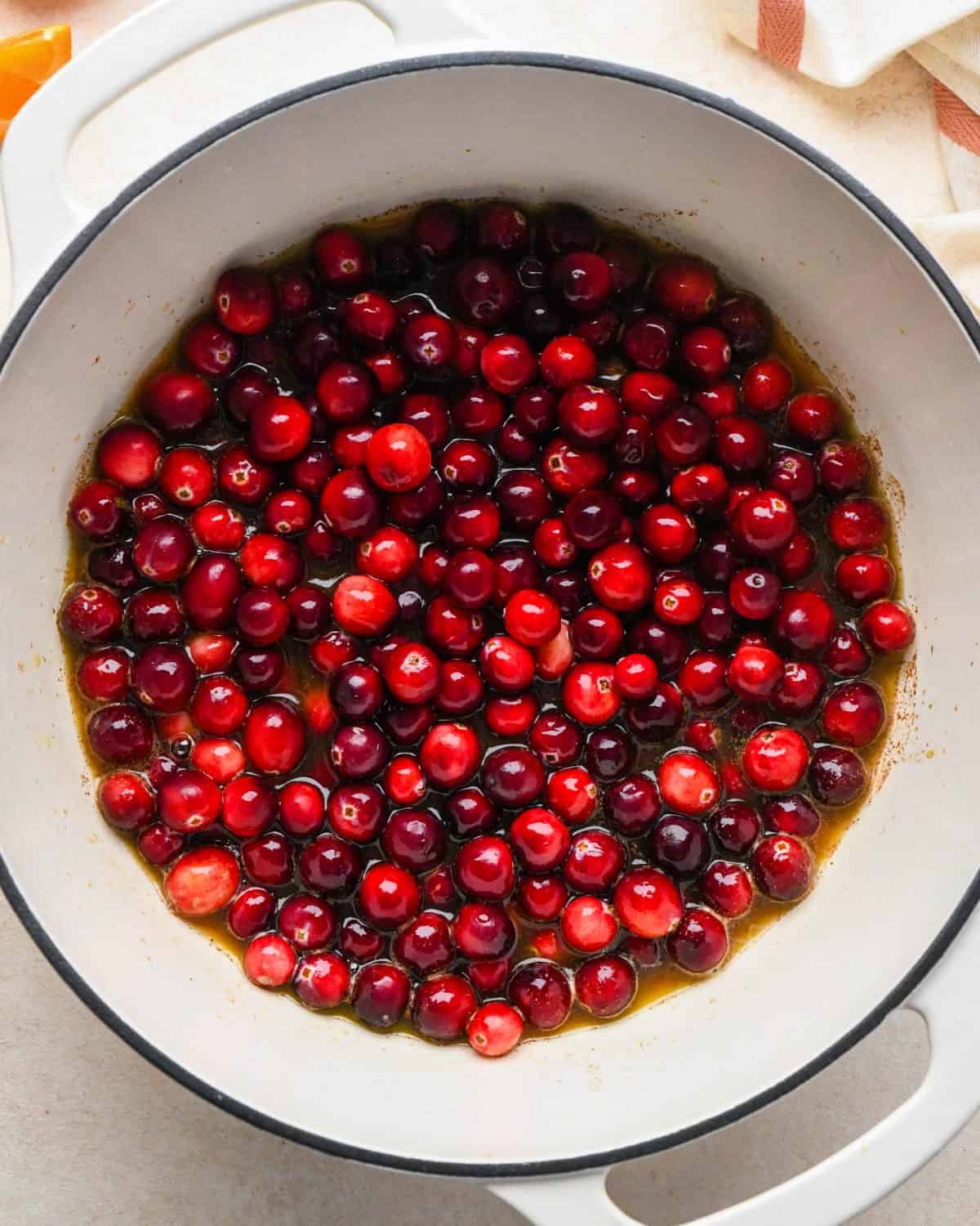 how to make cranberry sauce - cranberries added to the orange juice mixture in a white pot wiht a black rim