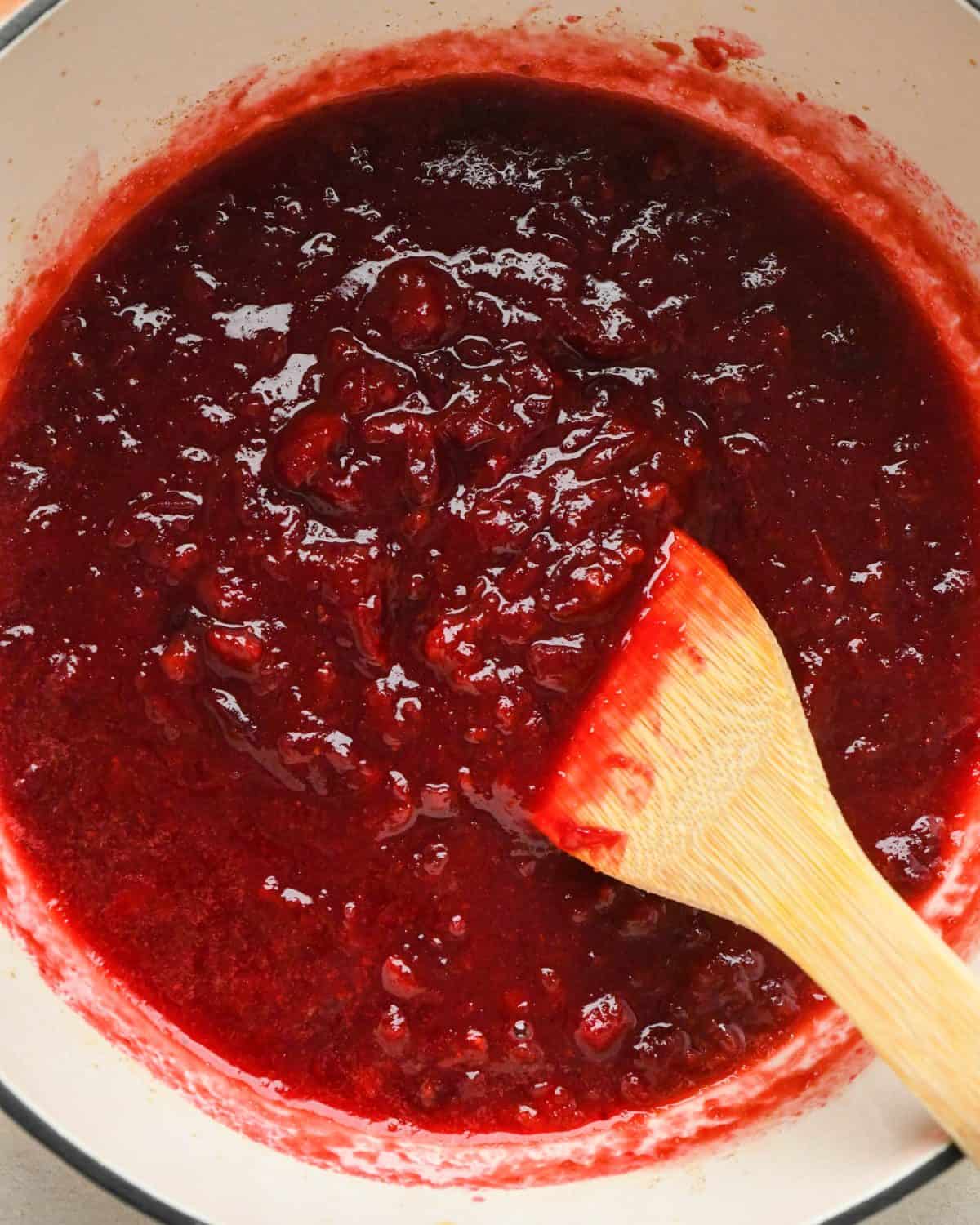 how to make cranberry sauce - a wooden spatula stirring the sauce as it cooks after being mashed