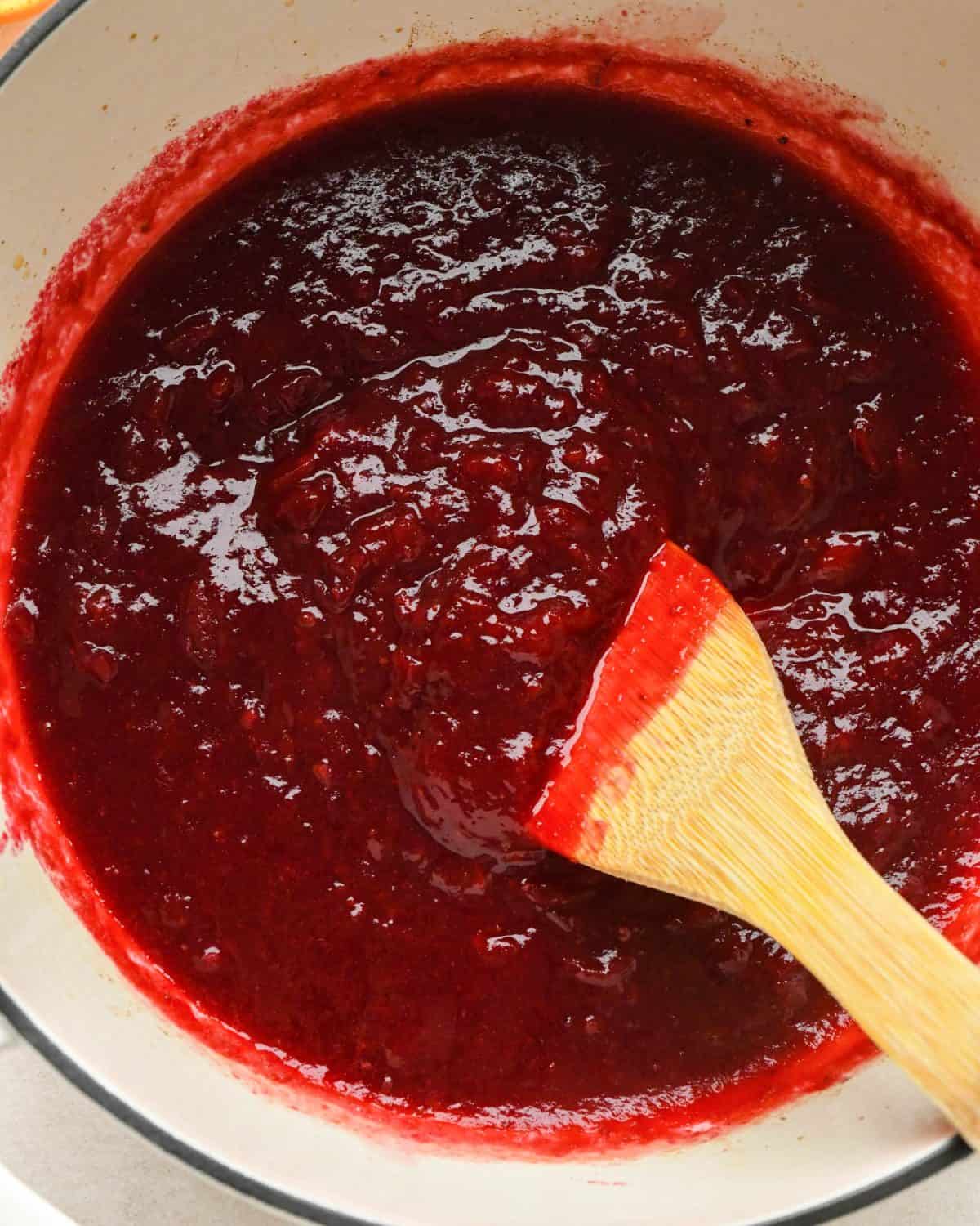 how to make cranberry sauce - a wooden spatula stirring the sauce as it cooks after being mashed showing the texture has thickened.