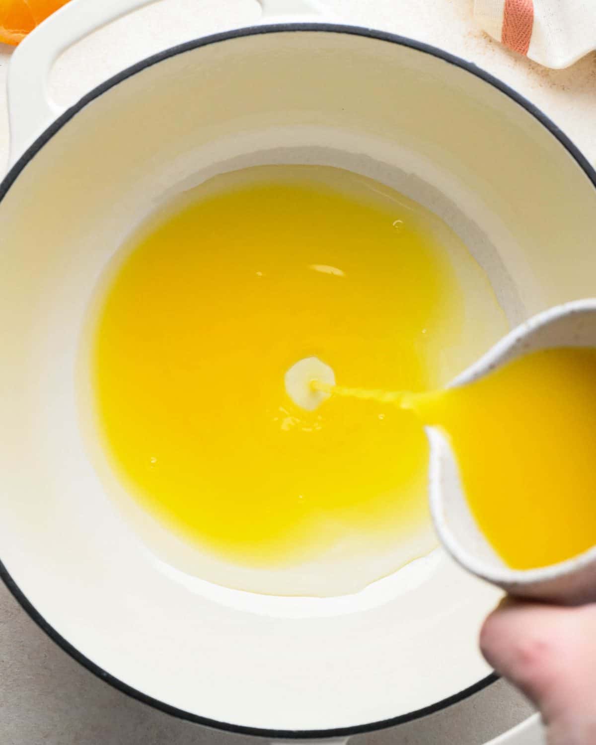 how to make cranberry sauce - orange juice being poured into a white pot with a black rim