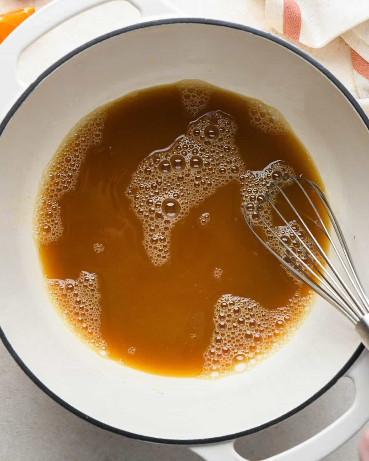 how to make cranberry sauce - both sugars added to orange juice in a white pot with a black rim after being whisked together, there's a metal whisk in the pot