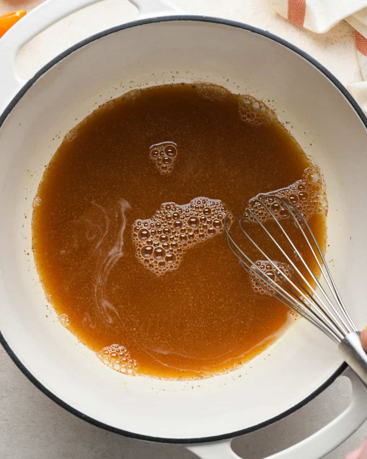 how to make cranberry sauce - cinnamon being whisked into the orange juice mixture in a white pot with a black rim.