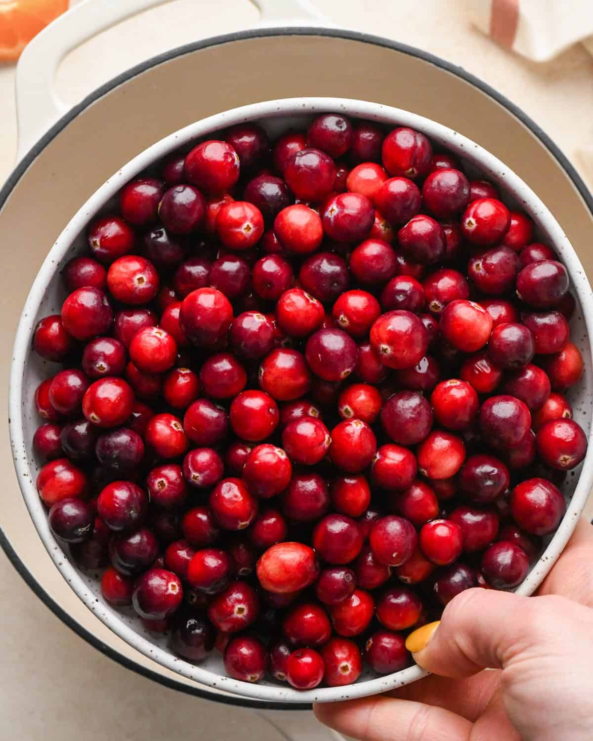 how to make cranberry sauce - a bowl of cranberries being held over a white pot with a black rim