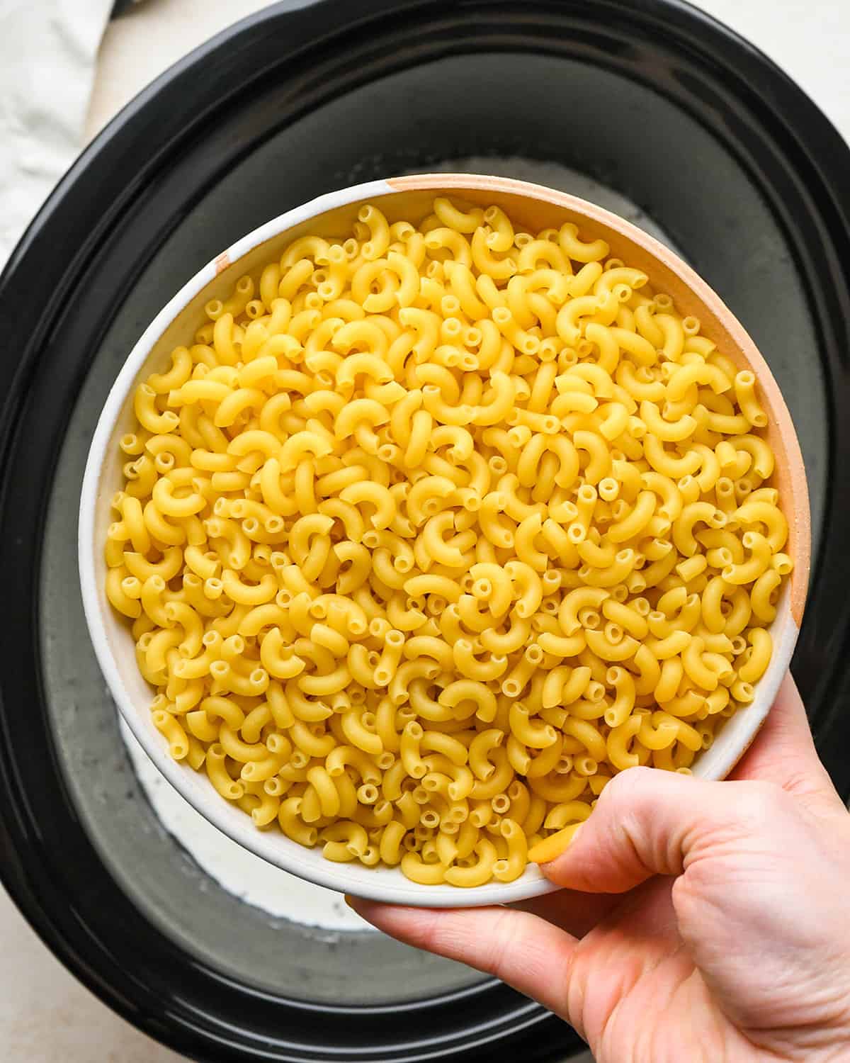 adding macaroni to the slow cooker to make crock pot macaroni and cheese