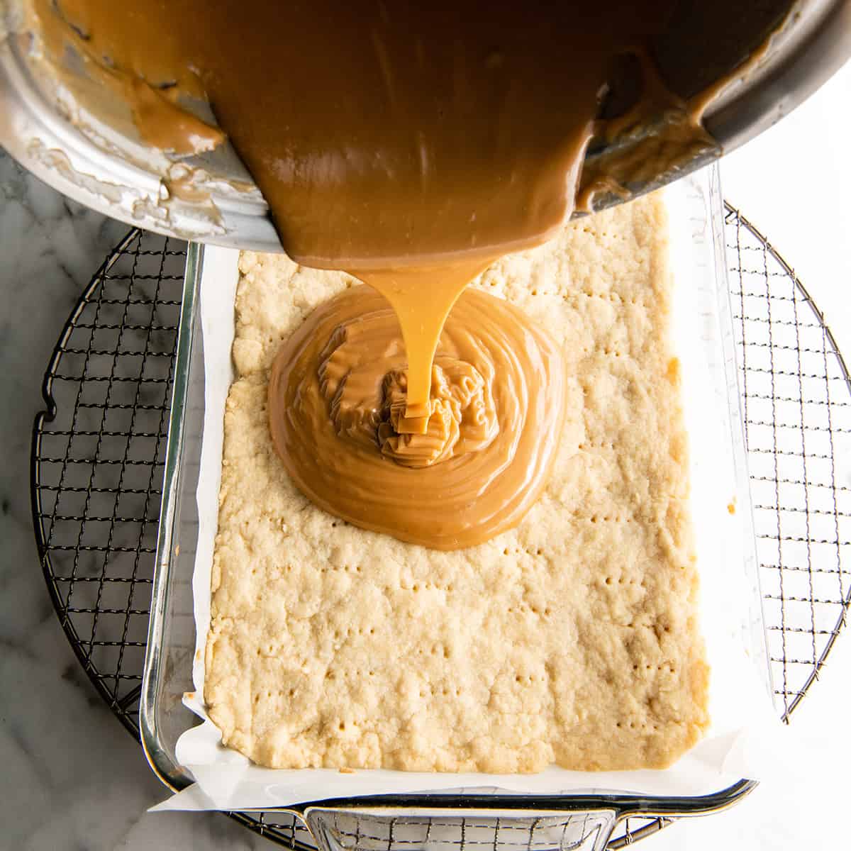 pouring caramel onto the shortbread layer of Millionaire Shortbread Bars