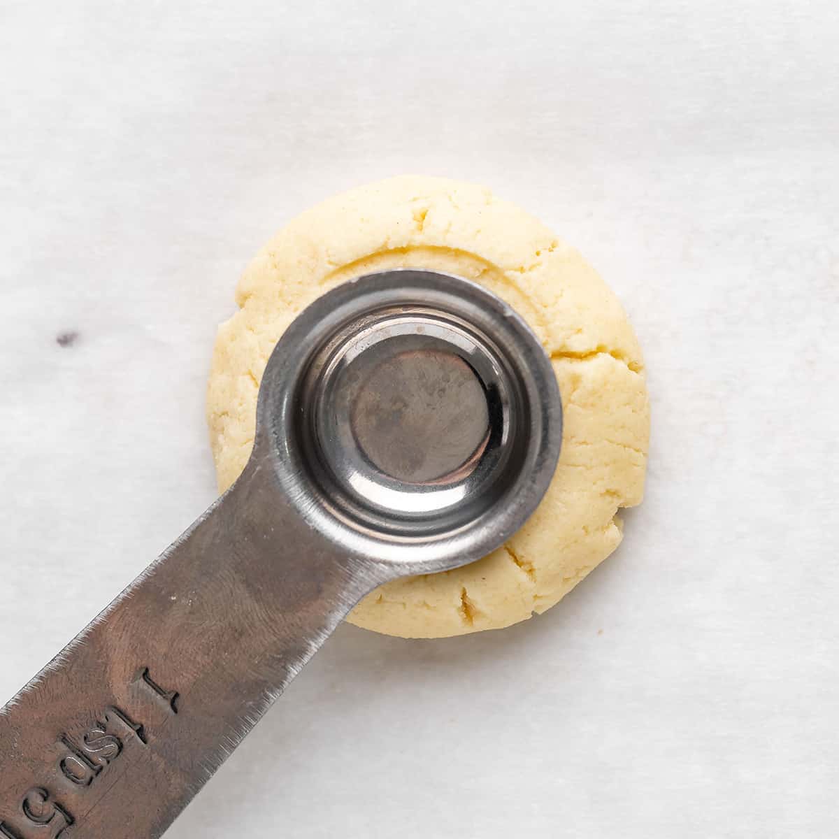 a teaspoon making a well in a ball of thumbprint cookie dough