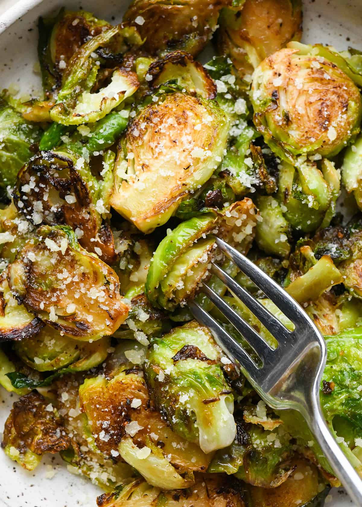 a fork taking a bite of Sautéed Brussels Sprouts on a plate topped with parmesan cheese