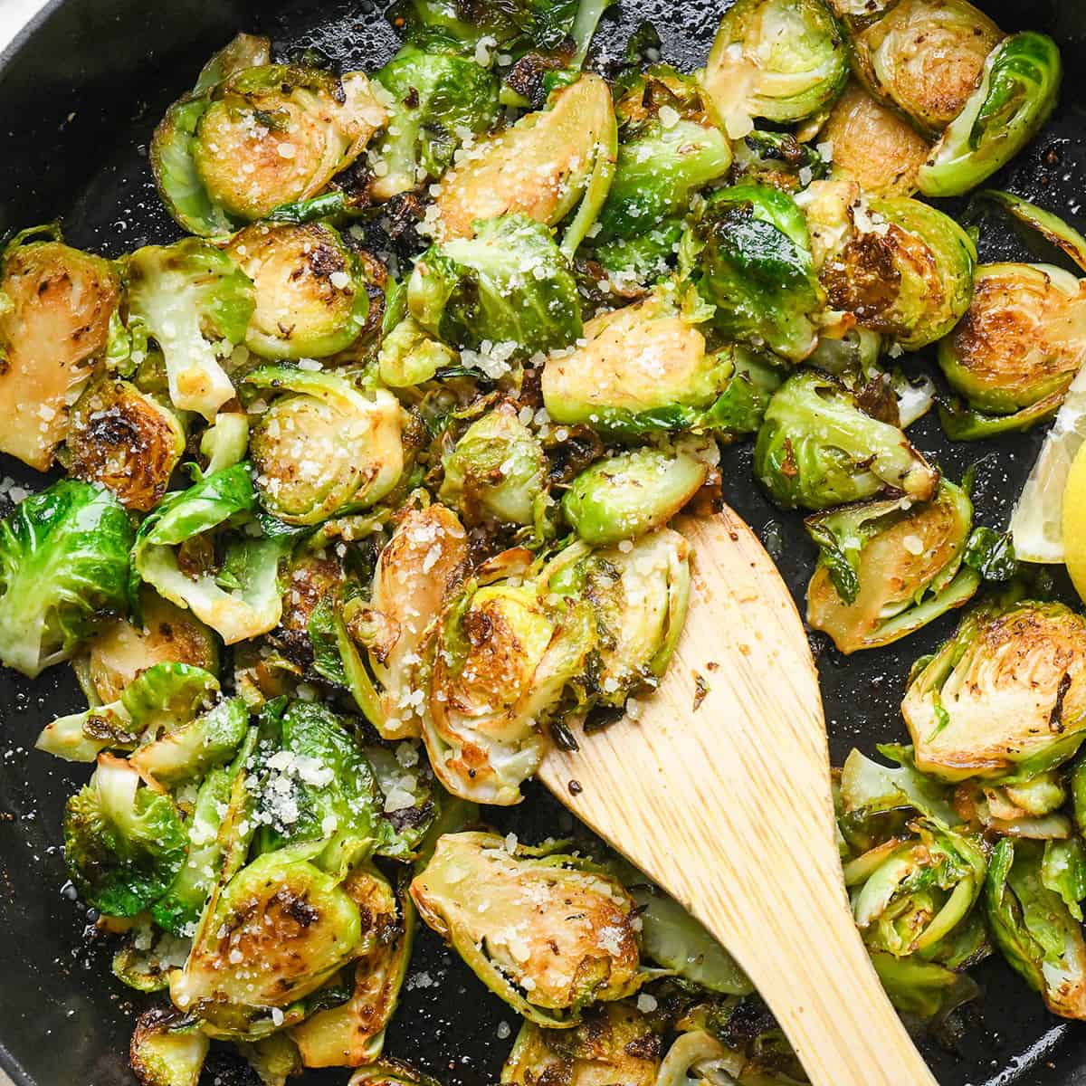 Sautéed Brussels Sprouts in a pan with a wooden spatula