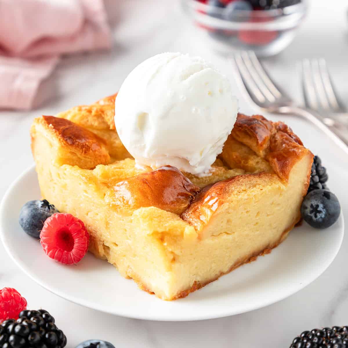 a slice of bread pudding on a plate topped with vanilla ice cream, garnished with berries