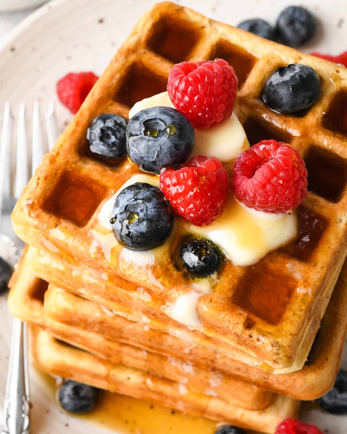 a stack of 5 homemade waffles topped with butter, syrup and berries