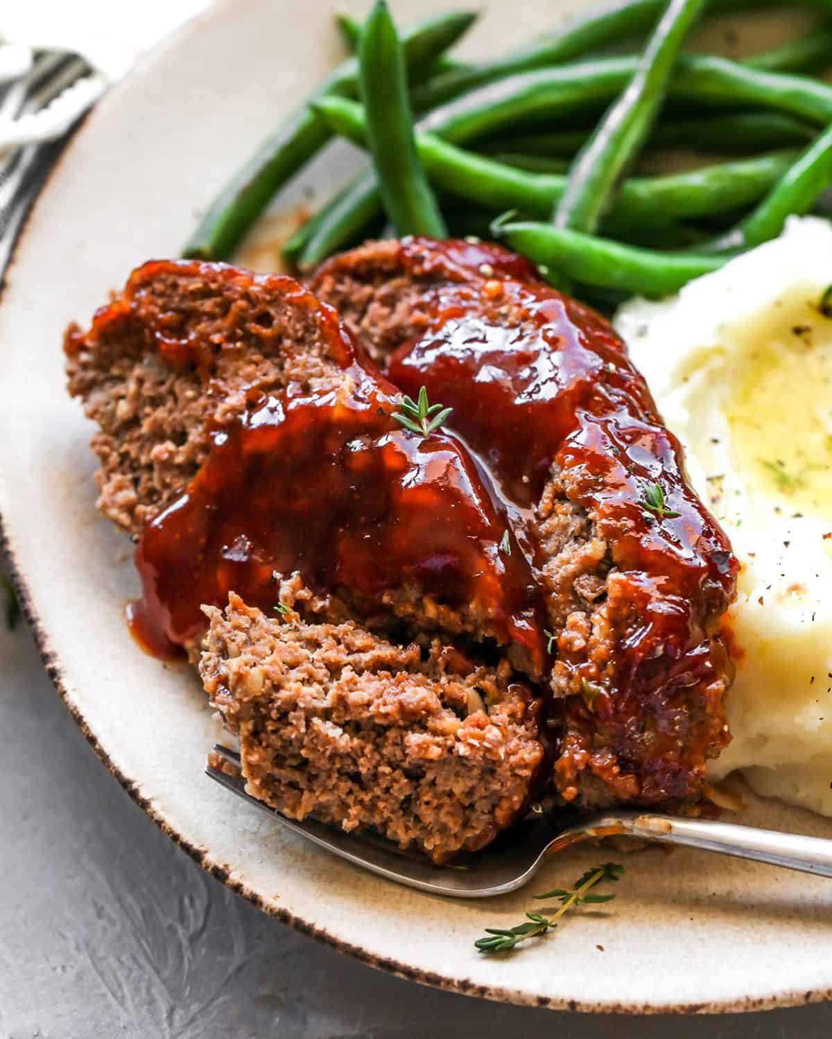two slices of the Best Meatloaf on a plate with beans and mashed potatoes and a fork. 