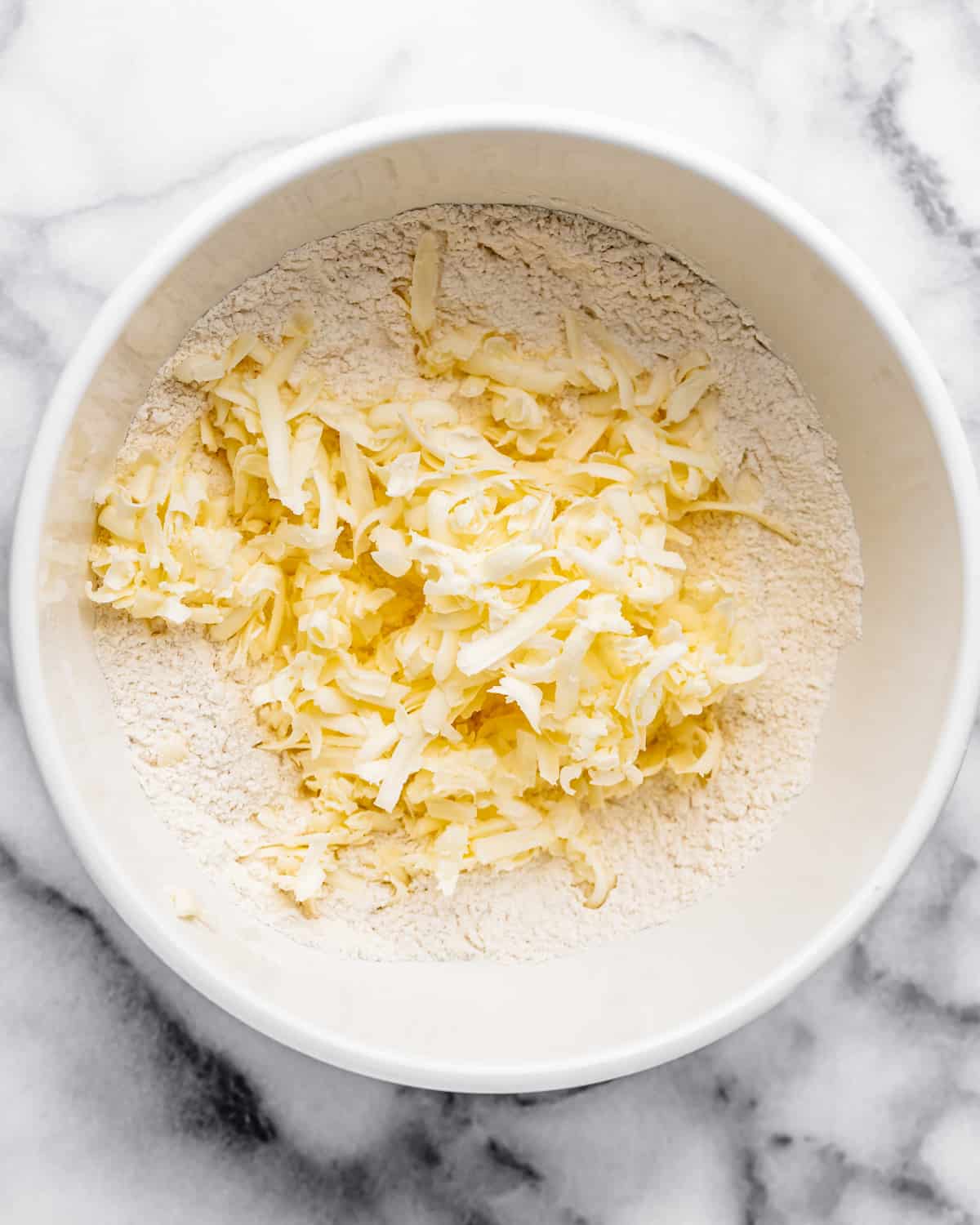 grated butter added to dry ingredients in a bowl before mixing